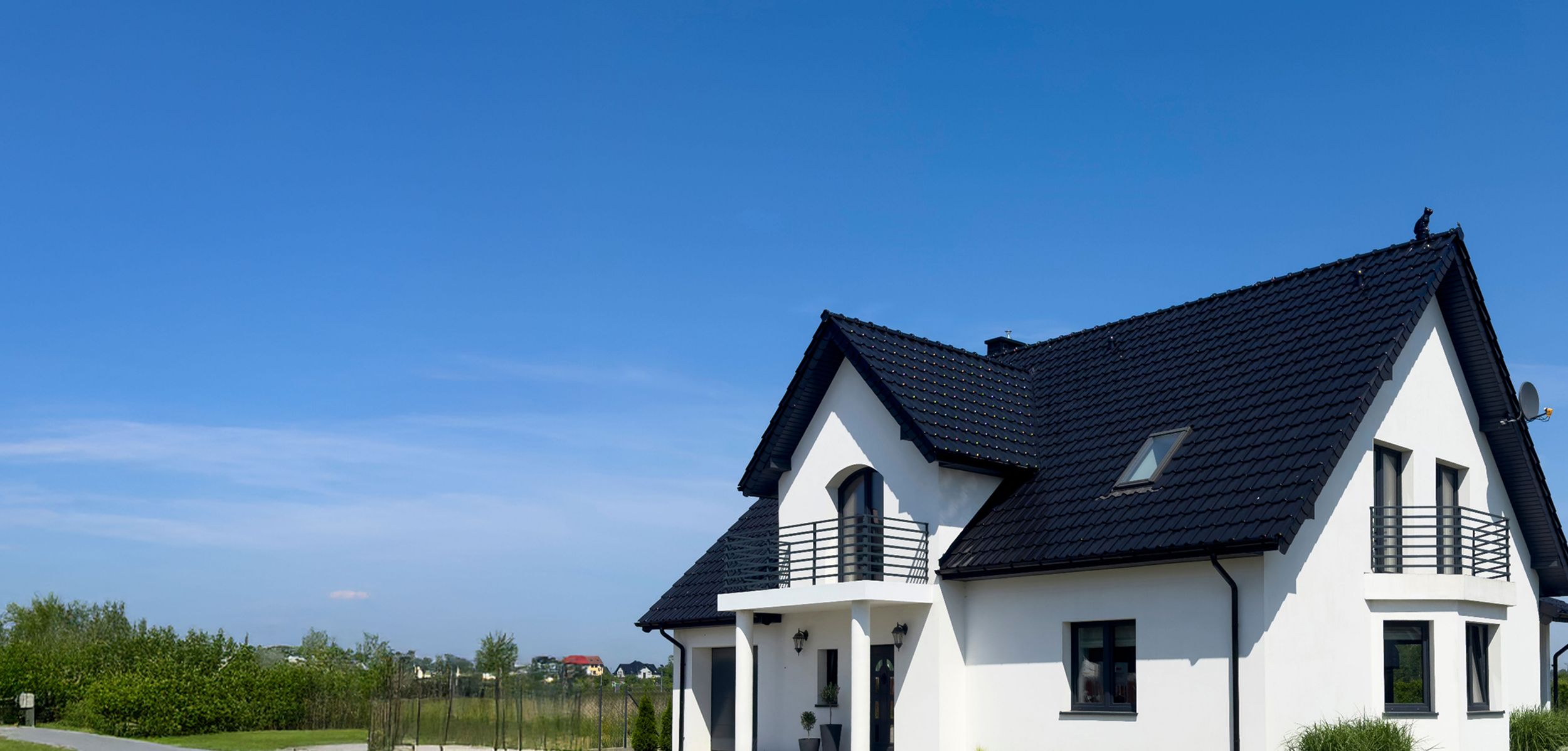 Weißes Haus mit schwarzen Dach, zwei Balkonen und blauer Himmel im Hintergrund